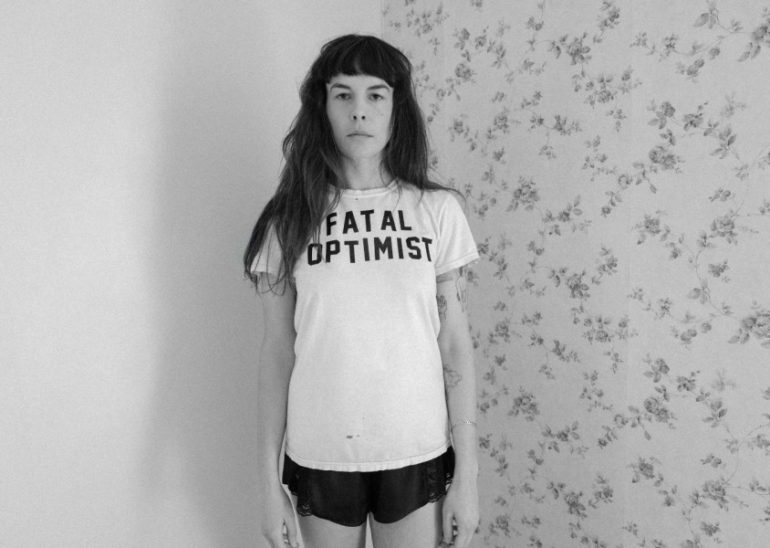 A black & white image of a woman stood in the corner of a roomx